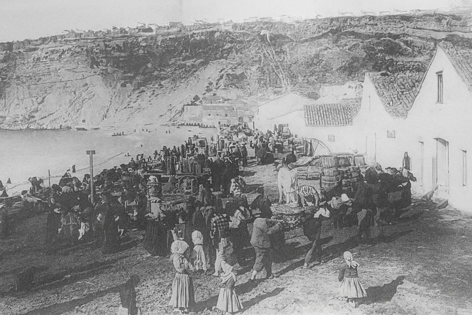 Scène ancienne à Nazaré avec pêcheurs et villageois au marché au pied de la falaise