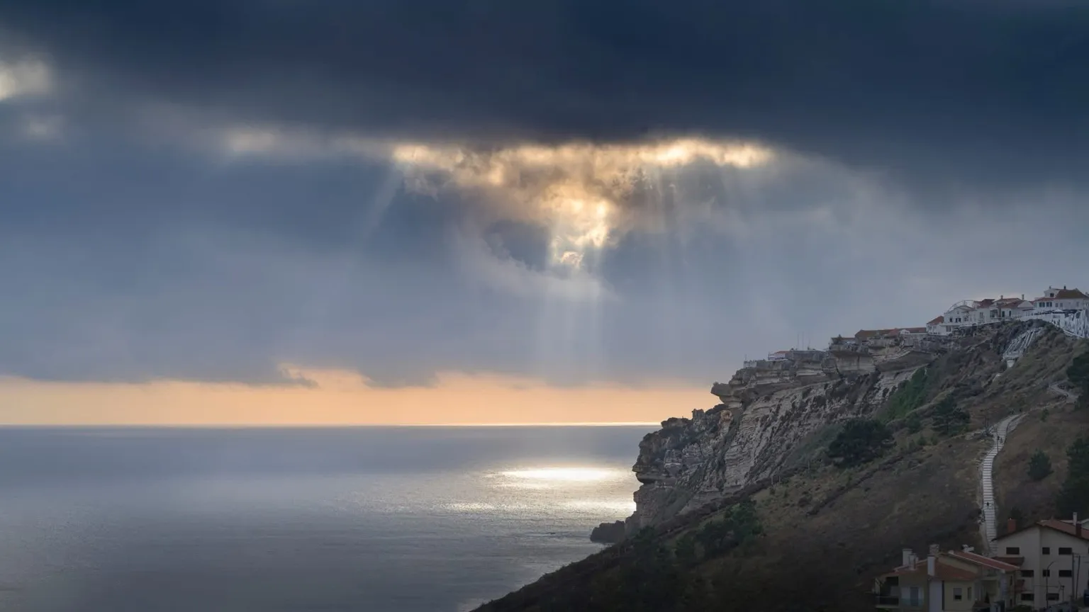 Falaises de Nazaré au coucher du soleil avec percée lumineuse dans les nuages